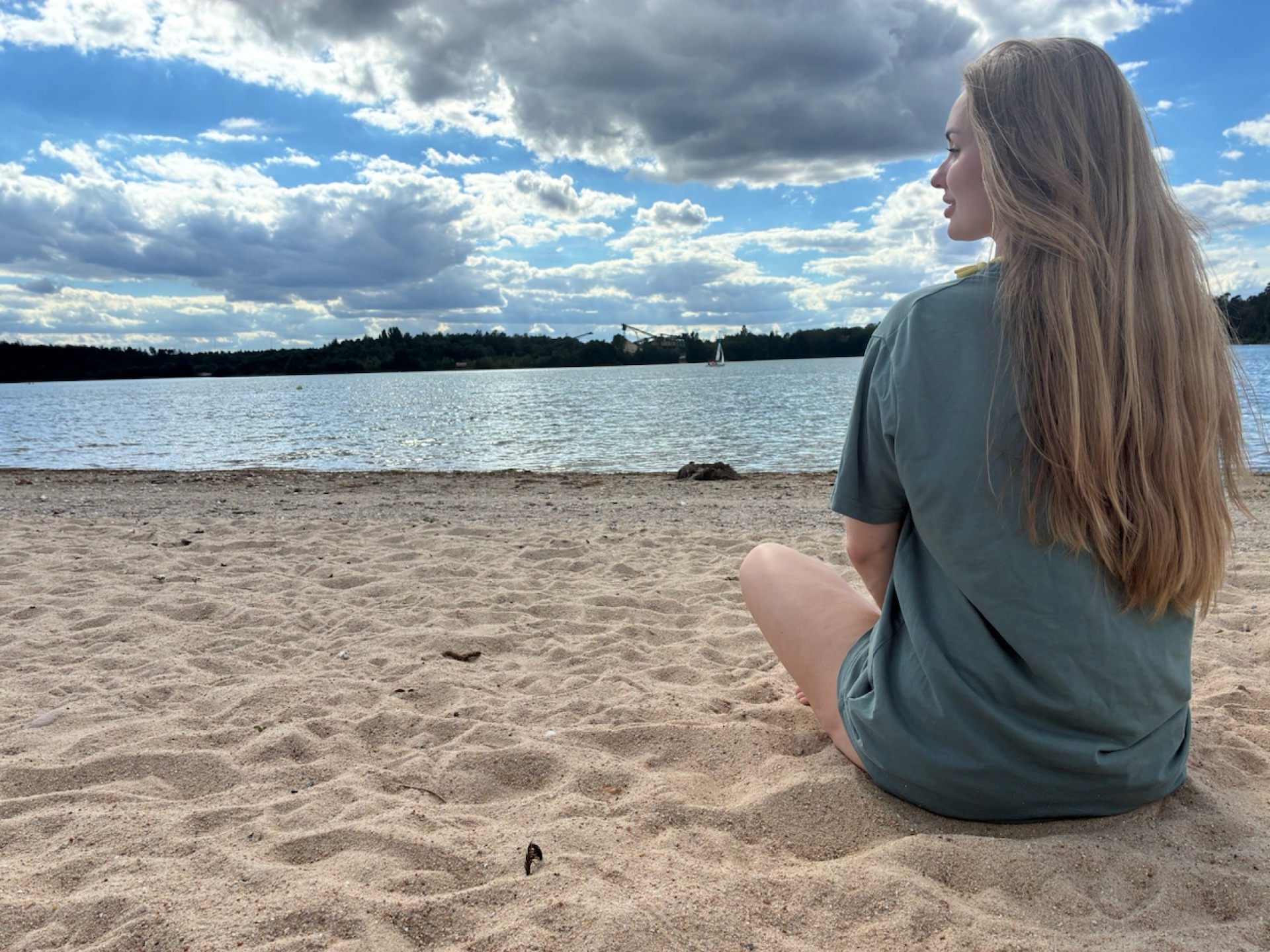 Woman sitting on a beach, looking out at the water and sky